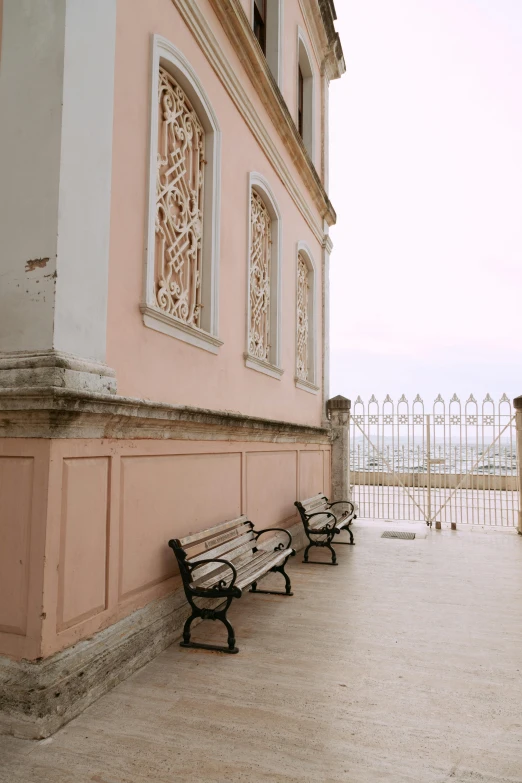 a couple of benches sitting in front of a building, inspired by Luis Paret y Alcazar, trending on unsplash, baroque, seaview, pink marble building, low quality photo, ( ( railings ) )