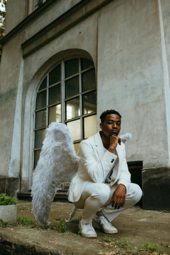 a man in a white suit sitting in front of a building, pexels contest winner, renaissance, feathery wings, 2 1 savage, cupid, high quality photo