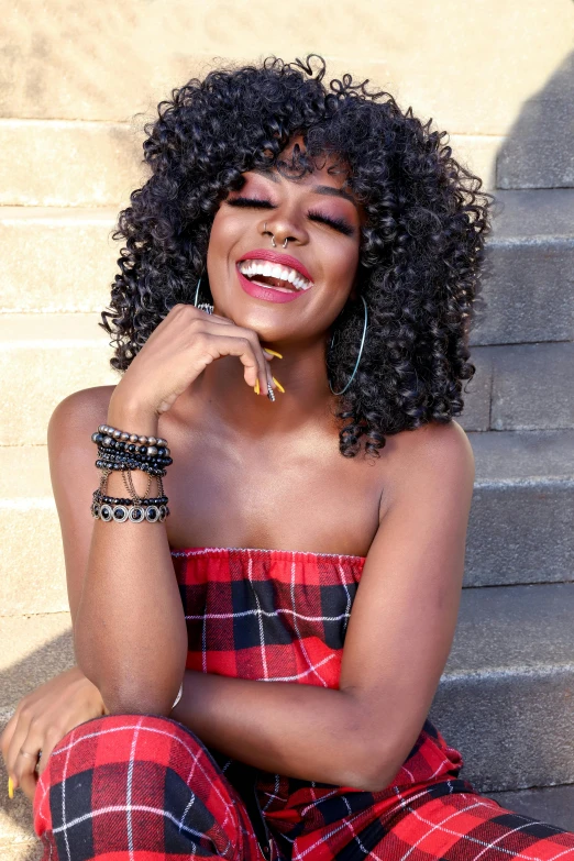 a woman sitting on the steps of a building, by Bernie D’Andrea, trending on pexels, happening, dark short curly hair smiling, sza, black jewelry, square