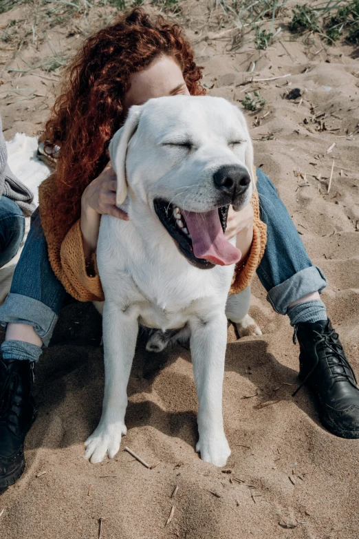 a woman sitting next to a white dog on top of a sandy beach, trending on pexels, renaissance, highly detailed photo of happy, pits, lesbians, soft lulling tongue