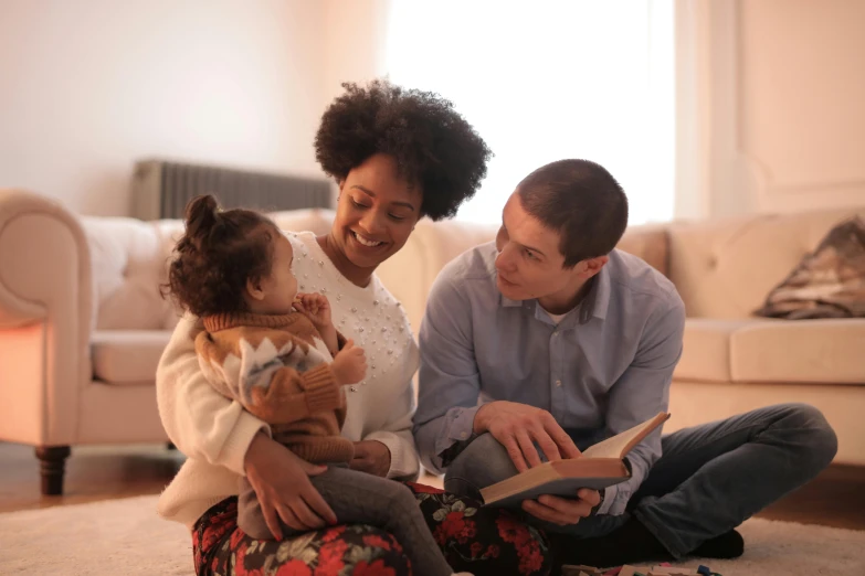 a man and woman sitting on the floor reading a book, a portrait, by Carey Morris, pexels, with a kid, avatar image, mixed race, brown