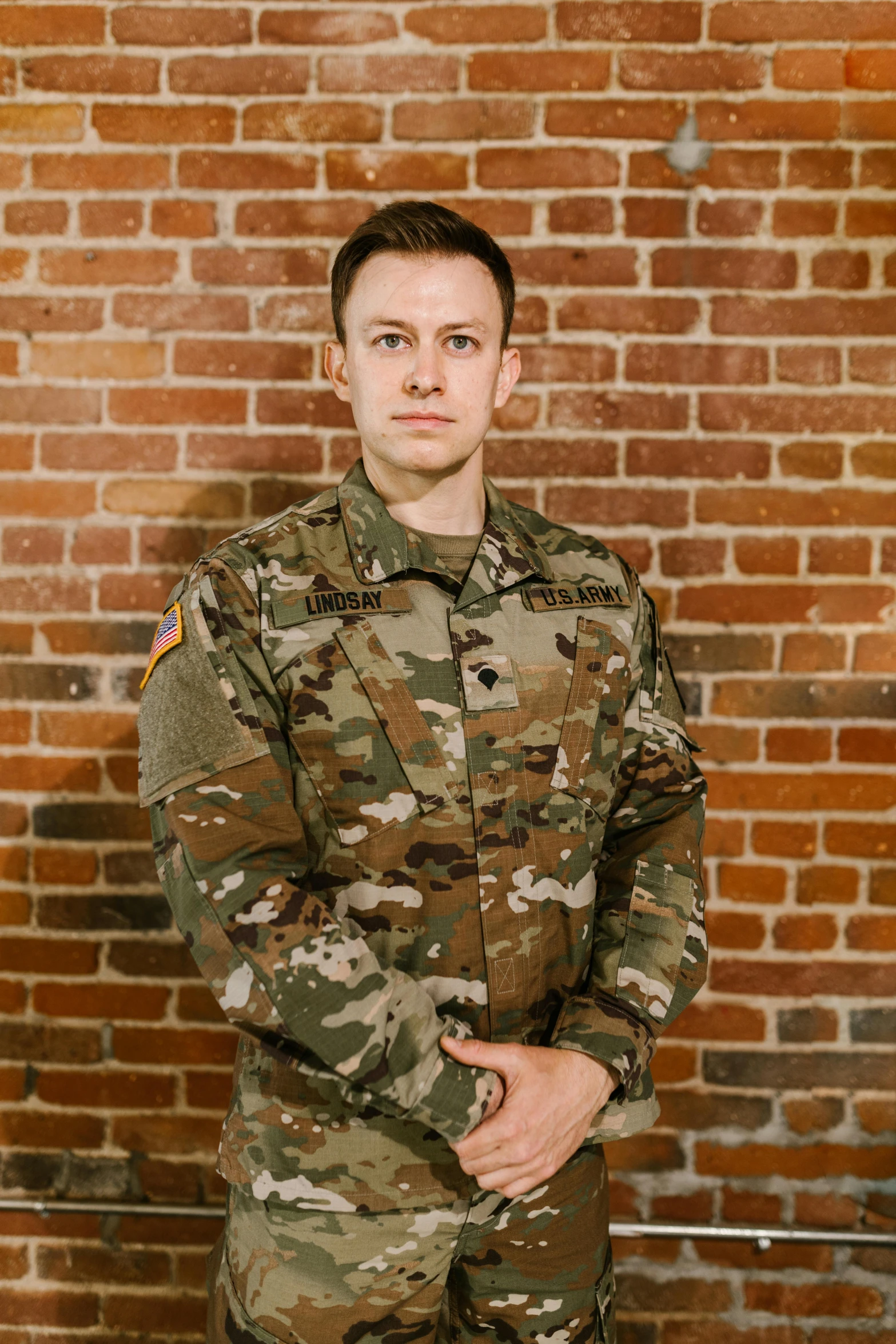 a soldier standing in front of a brick wall, a portrait, reddit, non-binary, adam varga, multicam (camo), official photo