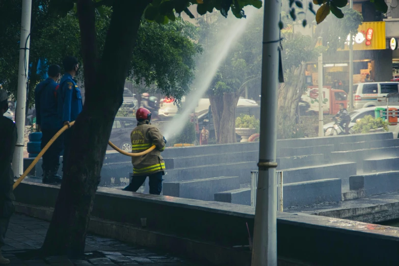 a fireman using a hose to put out a fire, by Alejandro Obregón, pexels contest winner, mexico city, avatar image, parks and public space, cctv footage of a movie set