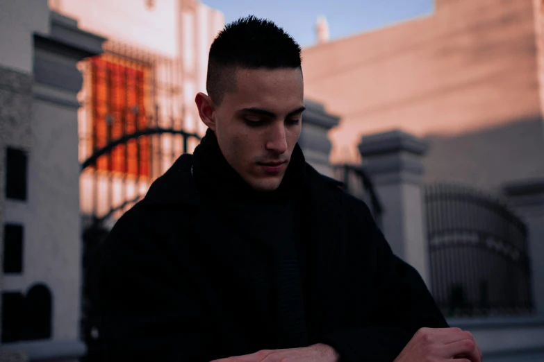 a man in a black coat looking down at his watch, an album cover, inspired by Carlos Berlanga, pexels contest winner, young handsome pale roma, street pic, people with mohawks, sitting in a cemetery at night