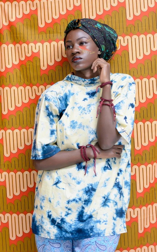 a woman standing in front of a colorful wall, inspired by Makoto Aida, trending on pexels, afrofuturism, wearing a tie-dye shirt, wearing an old tunic, high angle closeup portrait, adut akech