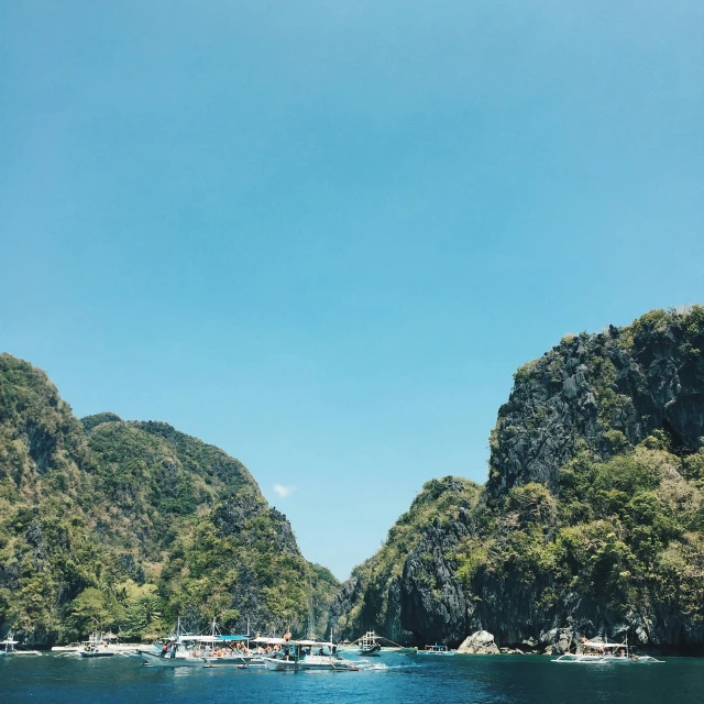 a group of boats floating on top of a body of water, by Robbie Trevino, pexels contest winner, island with cave, clear blue sky vintage style, 1970s philippines, view from below