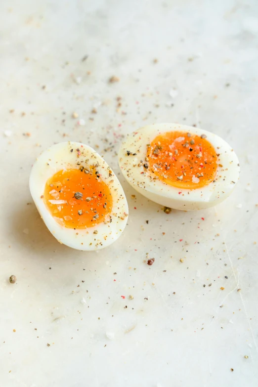 a couple of eggs sitting on top of a counter, hard boiled, smooth tiny details, white and orange, pepper