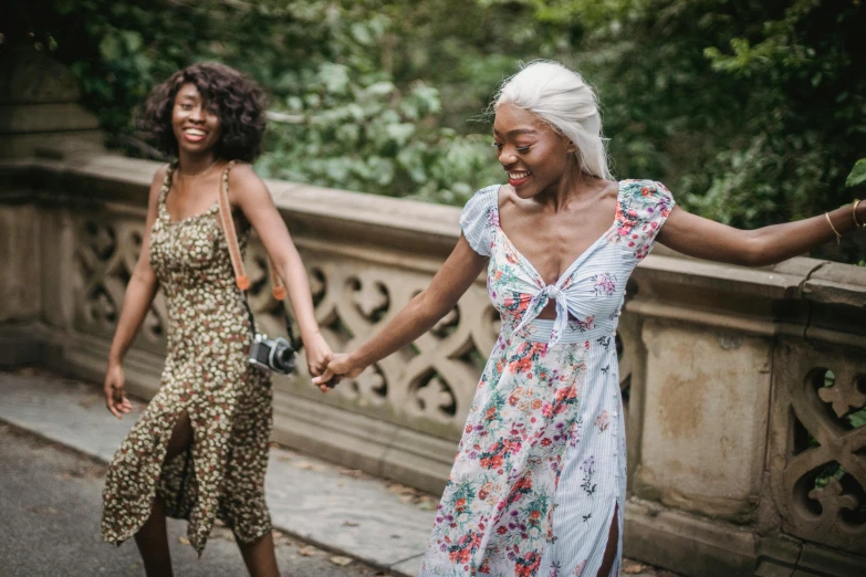 two women walking across a bridge holding hands, pexels contest winner, happening, black young woman, smiling and dancing, central park, wearing in a summer dress