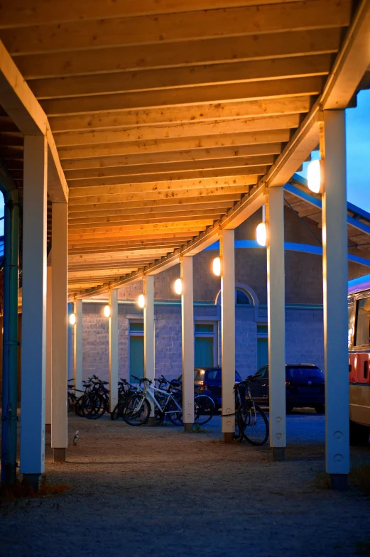 a row of parked bikes under a covered walkway, by Jens Søndergaard, evening lighting, wooden structures, fzd school of design, square