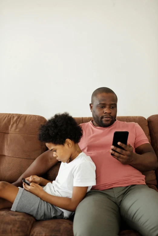 a man and a boy sitting on a couch looking at a cell phone, incoherents, jemal shabazz, fatherly, bl