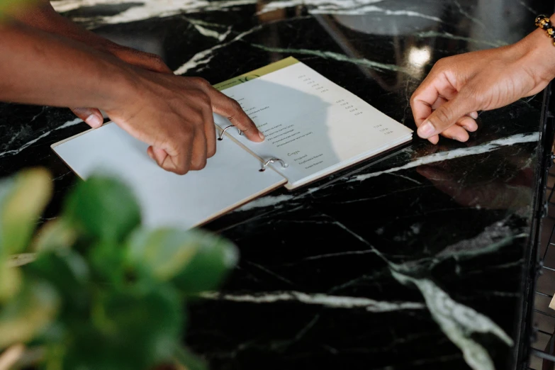 a couple of people that are sitting at a table, by Carey Morris, pexels contest winner, black marble, holding notebook, detailed information, ignant