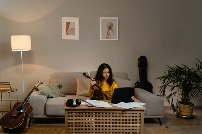 a woman sitting on a couch playing a guitar, by Julia Pishtar, pexels contest winner, working on a laptop at a desk, standing on top of a violin, ameera al-taweel, small and cosy student bedroom