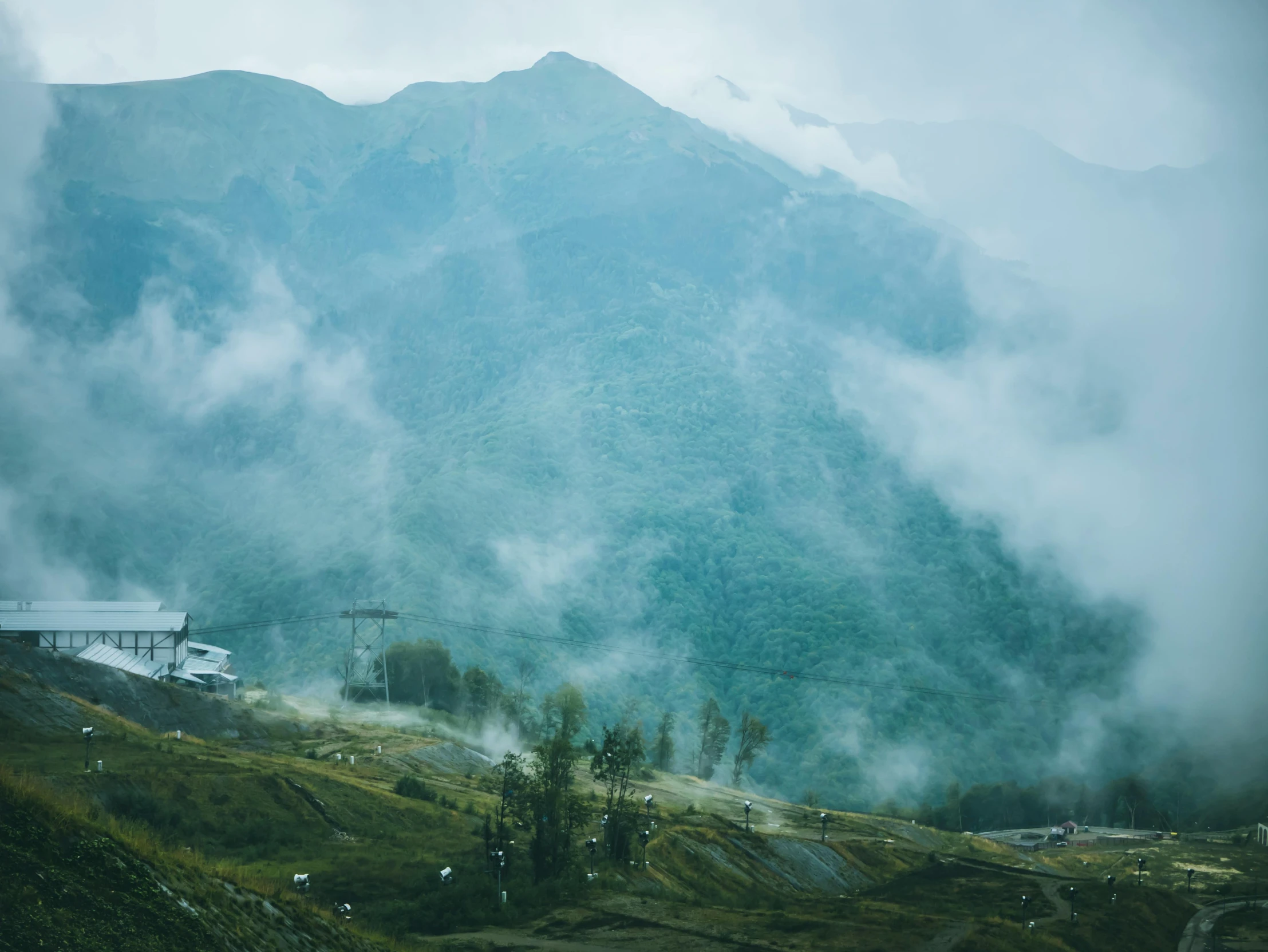 a view of a mountain covered in mist and clouds, by Muggur, pexels contest winner, hurufiyya, chairlifts, lush forest in valley below, background image, [ cinematic