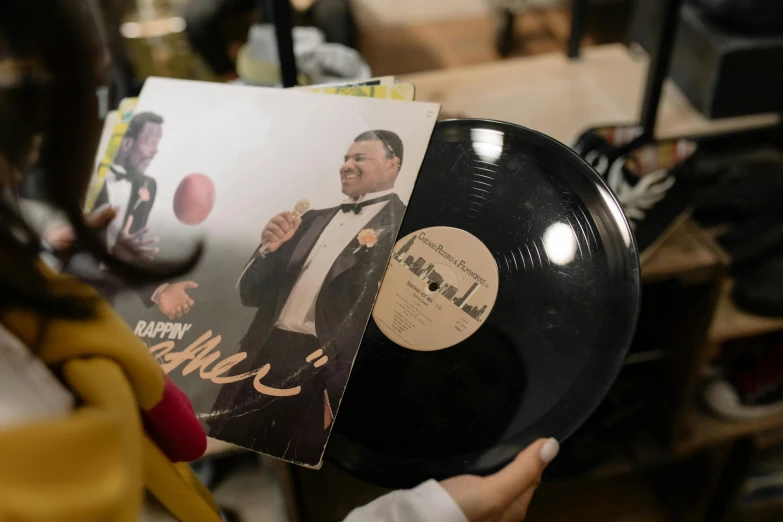 a person holding a record with a picture of a man in a tuxedo, by Julia Pishtar, pexels contest winner, harlem renaissance, product display photograph, 🌻🎹🎼, vinyl cut ready, big floppa