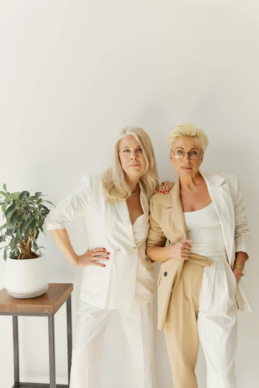 a couple of women standing next to each other, inspired by Irene and Laurette Patten, unsplash, minimalism, wearing white suit and glasses, white - blond hair, at home, earthy