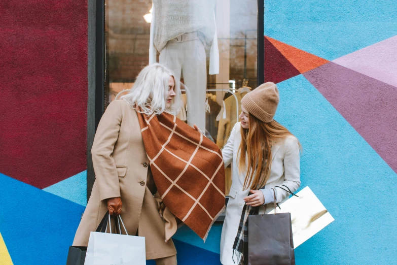 a couple of women standing next to each other holding shopping bags, pexels contest winner, maximalism, back of emma stone in beige coat, retaildesignblog, a cozy, wearing a brown cape