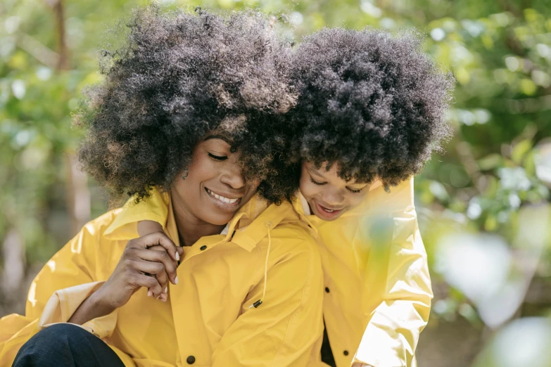 a couple of women sitting next to each other, a portrait, by Winona Nelson, pexels, yellow raincoat, with afro, daughter, hugging