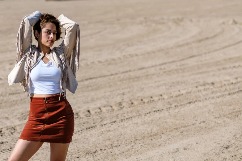 a woman standing on top of a sandy beach, a portrait, by Robbie Trevino, trending on pexels, mini skirt, on a desert road, background image, cropped shirt with jacket