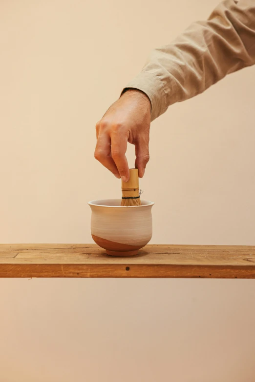 a person putting something in a bowl on a table, inspired by Hendrik Gerritsz Pot, natural wood top, vibrating, white, sake