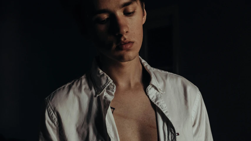 a shirtless man standing in a dark room, an album cover, inspired by Jean Malouel, pexels contest winner, hyperrealism, wearing a white button up shirt, cheekbones, androgynous person, profile pic