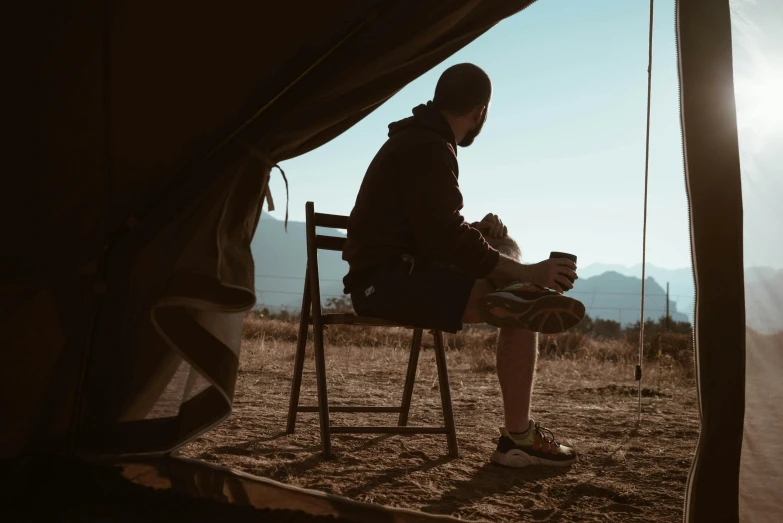 a man sitting in a chair outside of a tent, pexels contest winner, profile image, morning coffee, brown, rey