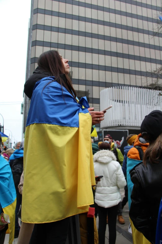 a group of people that are standing in the street, inspired by Júlíana Sveinsdóttir, antipodeans, ukrainian flag on the left side, wearing a king's cape, yellow and blue and cyan, quebec