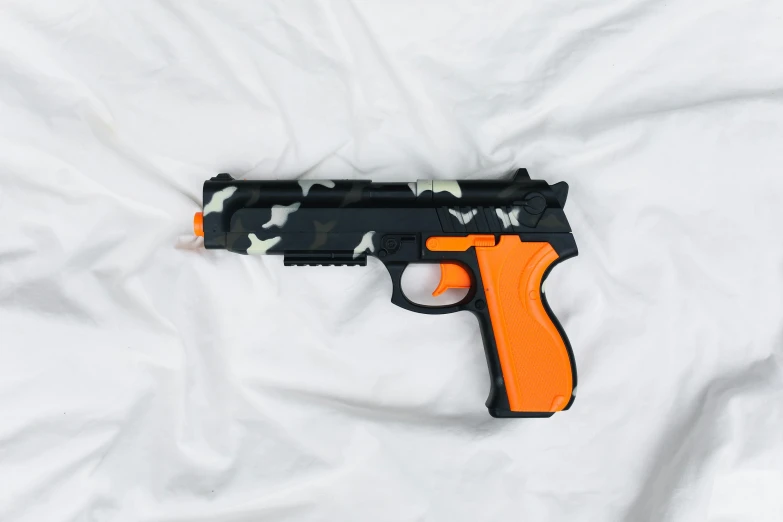a toy gun laying on top of a white sheet, orange and black, gen z, camouflage, item