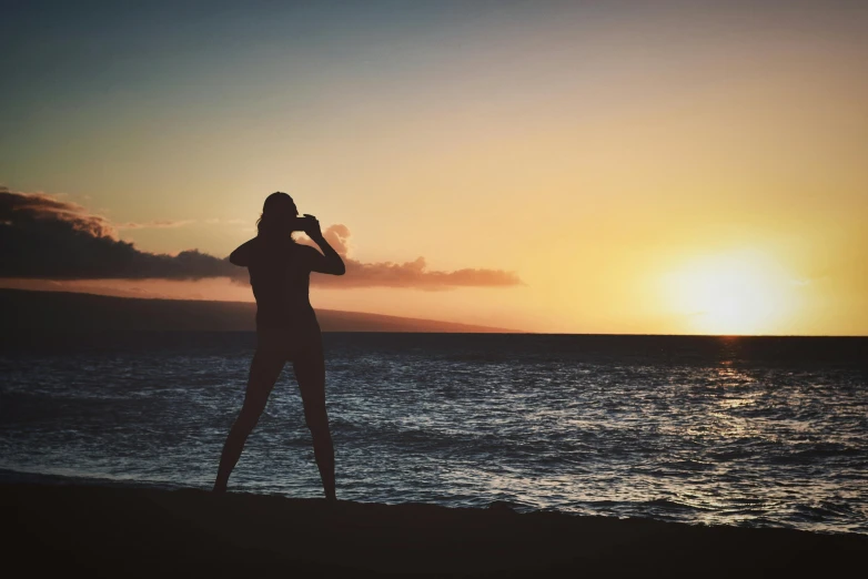 a woman standing on top of a beach next to the ocean, pexels contest winner, silhouette :7, maui, taking a picture, body shot