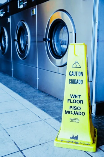 a wet floor sign in front of a row of washing machines, by Julia Pishtar, pexels, hispanic, thumbnail, worksafe. cinematic, cone shaped