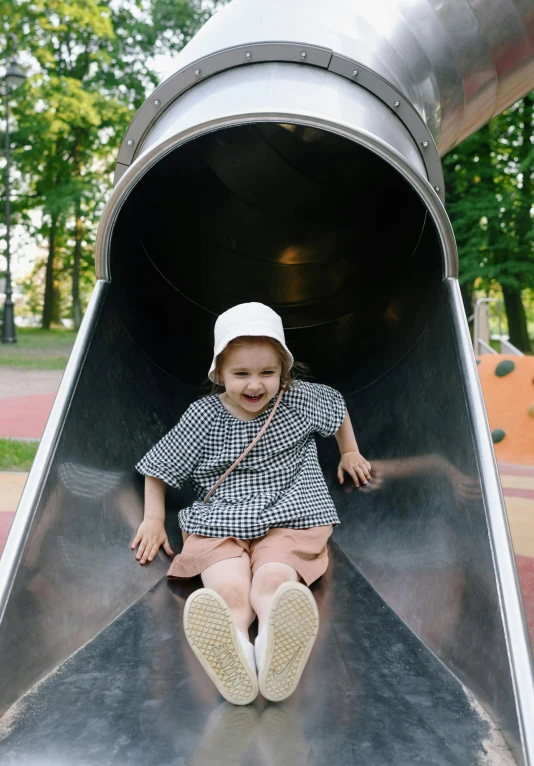 a little girl sitting on top of a metal slide, pexels contest winner, espoo, she is wearing a hat, grey, at a park