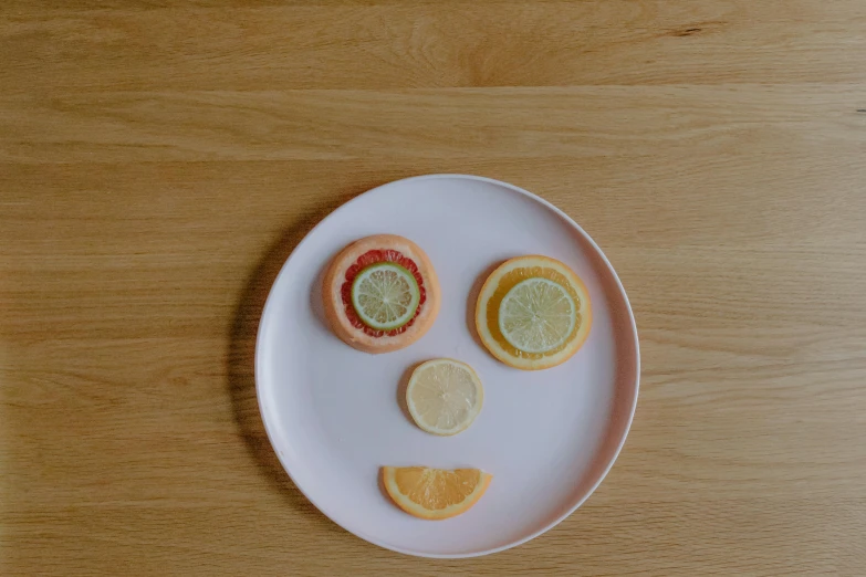 a white plate topped with slices of fruit, trending on unsplash, minimalism, highly detailed winking face, on a wooden plate, pink face, lemons