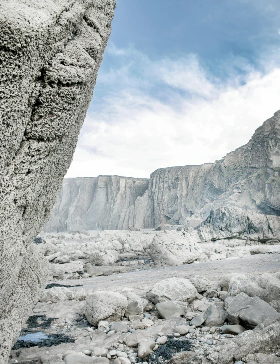 a man standing on top of a rock next to a river, a matte painting, inspired by Filip Hodas, unsplash contest winner, icy glaciers, made in tones of white and grey, between sedimentary deposits, gravel and scree ground