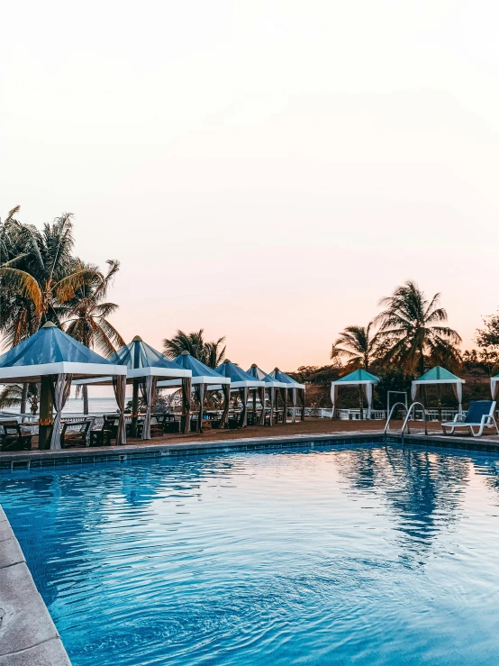 an empty swimming pool with lounge chairs and umbrellas, pexels contest winner, happening, sun down, next to a tropical pool, blue sky, bored ape yacht club