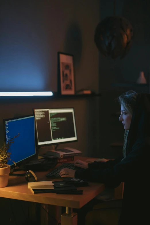 a woman sitting at a desk in front of two computer monitors, inspired by Elsa Bleda, pexels, hacking into the mainframe, nighttime, promo image, at home