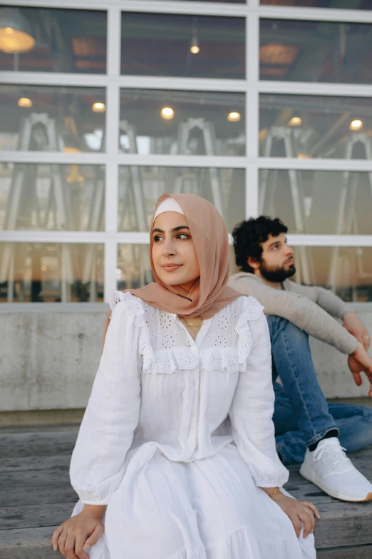 a woman sitting on a bench next to a man, by Maryam Hashemi, trending on pexels, hurufiyya, wearing white clothes, wearing a head scarf, casual pose, promotional image