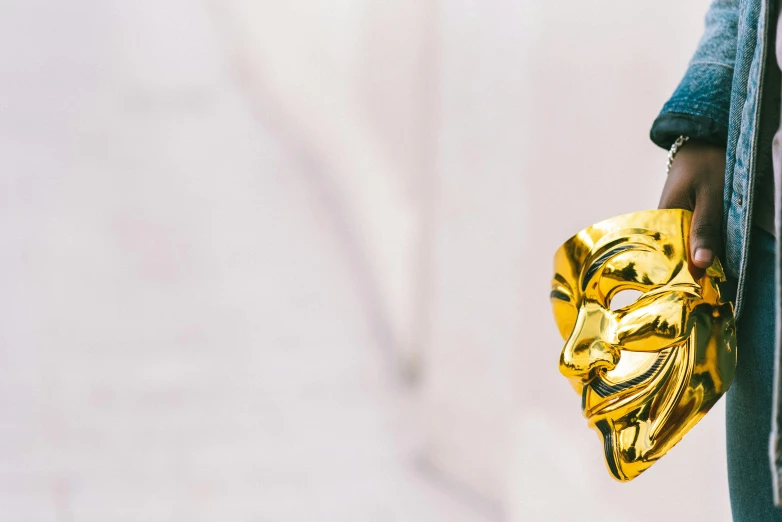 a person holding a gold mask in their hand, antipodeans, joker, winning award image, on a white table, avatar image