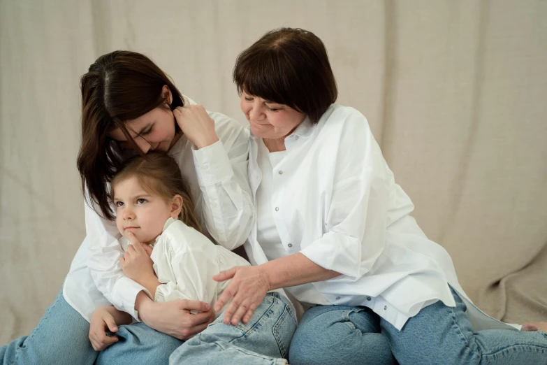 a woman sitting on top of a bed next to a little girl, by Attila Meszlenyi, pexels, white shirts, three women, hugging each other, soft but grumpy