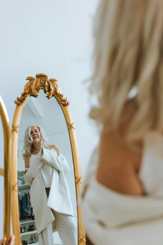 a woman that is standing in front of a mirror, a photo, by Julian Allen, trending on unsplash, rococo, white and gold robes, platinum blond, white cape, looking happy