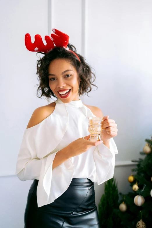 a woman holding a glass of wine in front of a christmas tree, featured on instagram, renaissance, wearing a cute top, mixed race woman, glossy white, photoshoot for skincare brand