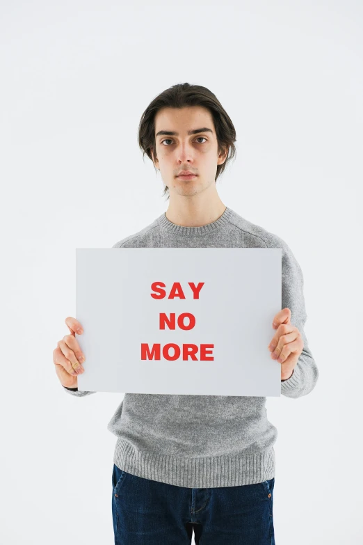 a man holding a sign that says say no more, an album cover, by Nicolette Macnamara, shutterstock, male model, riccardo scamarcio, no - text no - logo, environment