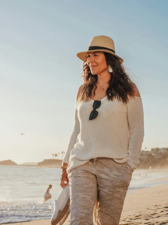 a woman walking on a beach next to the ocean, beige fedora, plus size woman, wearing casual sweater, avatar image