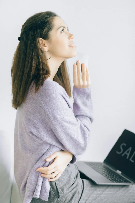 a woman sitting on a bed in front of a laptop, trending on pexels, renaissance, wearing a cardigan, waist reaching ponytail, lilac, advertising photo
