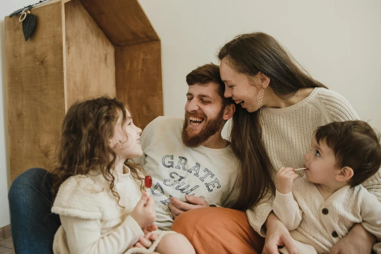 a man sitting on top of a couch next to a woman and two children, pexels contest winner, earing a shirt laughing, brown beard, avatar image, 1 2 9 7