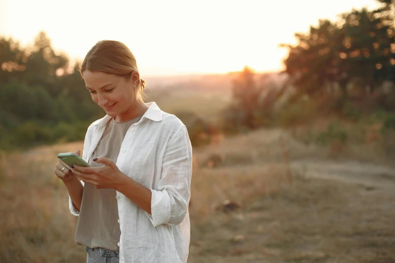 a woman standing in a field looking at her cell phone, trending on pexels, wearing a linen shirt, avatar image, white, reading