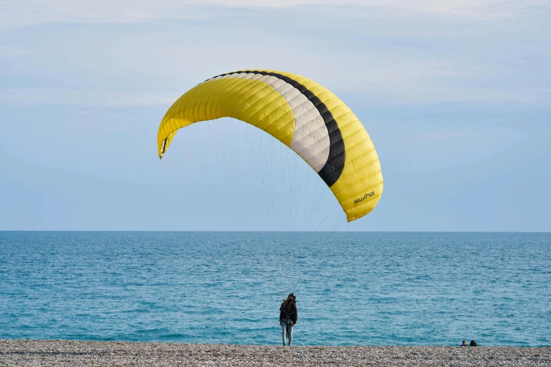 a person standing on a beach flying a kite, yellow and black, picton blue, parachutes, lightweight