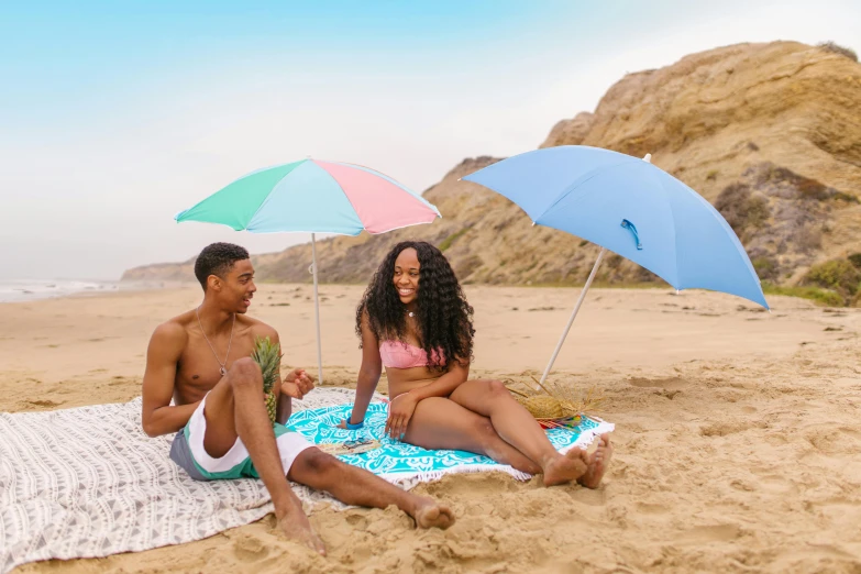 a couple of people sitting on top of a sandy beach, colorful umbrella, photoshoot for skincare brand, teenage vanessa morgan, on a canva