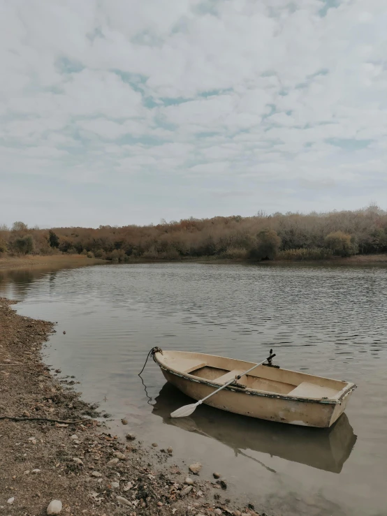 a small boat sits on the shore of a lake, by Elsa Bleda, pexels contest winner, renaissance, hollister ranch, the thames is dry, low quality photo, pembrokeshire