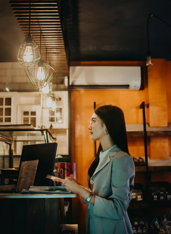 a woman standing in front of a laptop computer, a screenshot, trending on pexels, cafe lighting, profile pic, asian women, at the counter