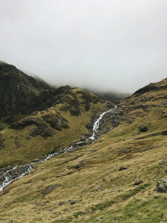 a herd of sheep standing on top of a lush green hillside, a picture, by Jessie Algie, waterfall. fog, crib goch!!!!!!!!!!! ridge, river running through it, overcast skies