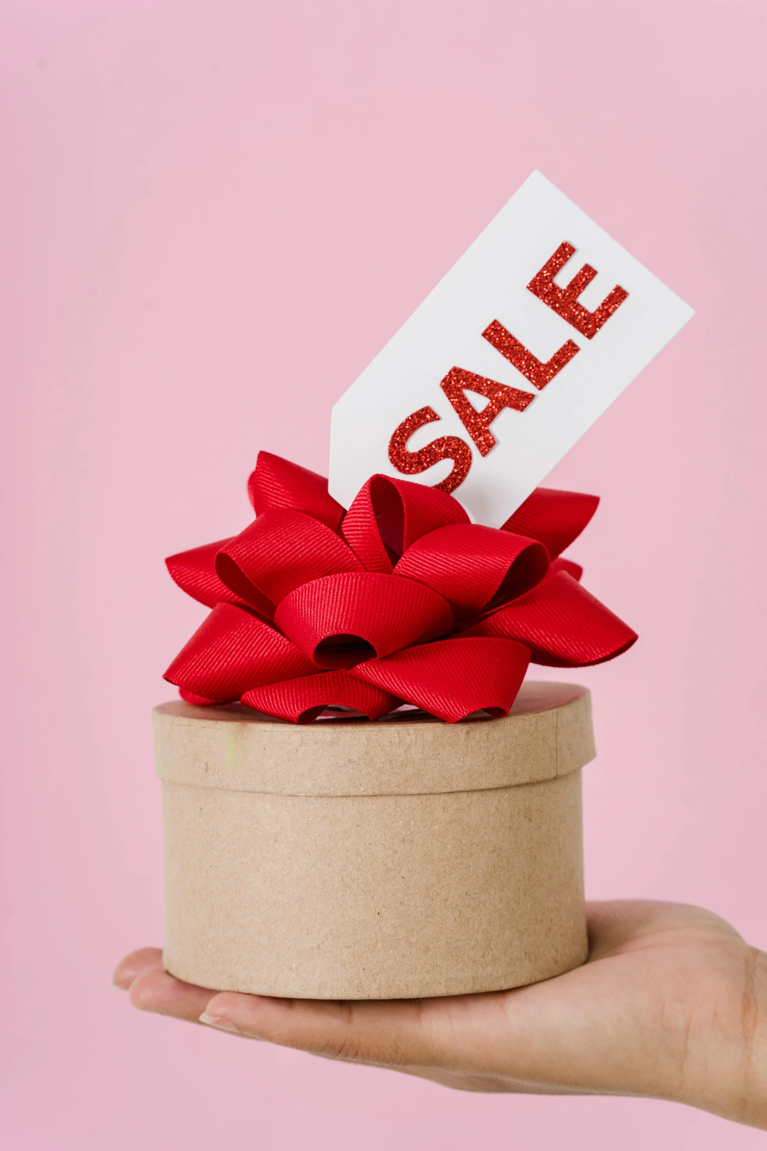 a person holding a box with a sale sign on it, a stock photo, by Gwen Barnard, trending on unsplash, magic realism, ornamental bow, pink, holiday, pot